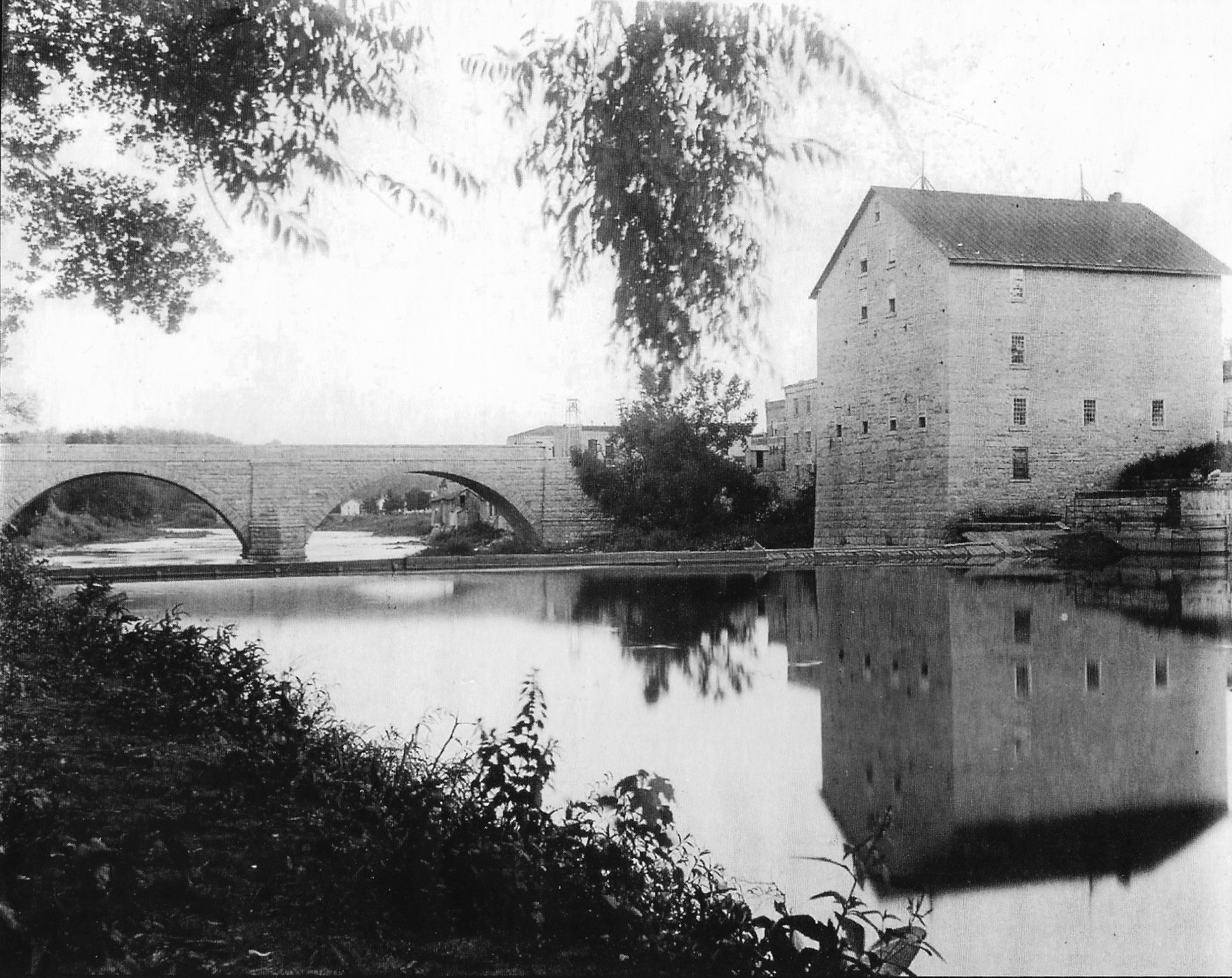 The stone mill and the Keystone Bridge reflected in the Turkey River, 1899